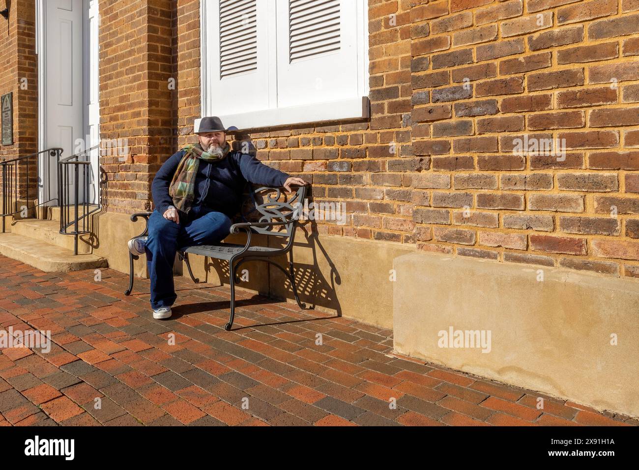 Un uomo che indossa un cappello e una sciarpa con la barba siede su una panchina di metallo nel centro storico di Greenville, Tennessee, Stati Uniti Foto Stock