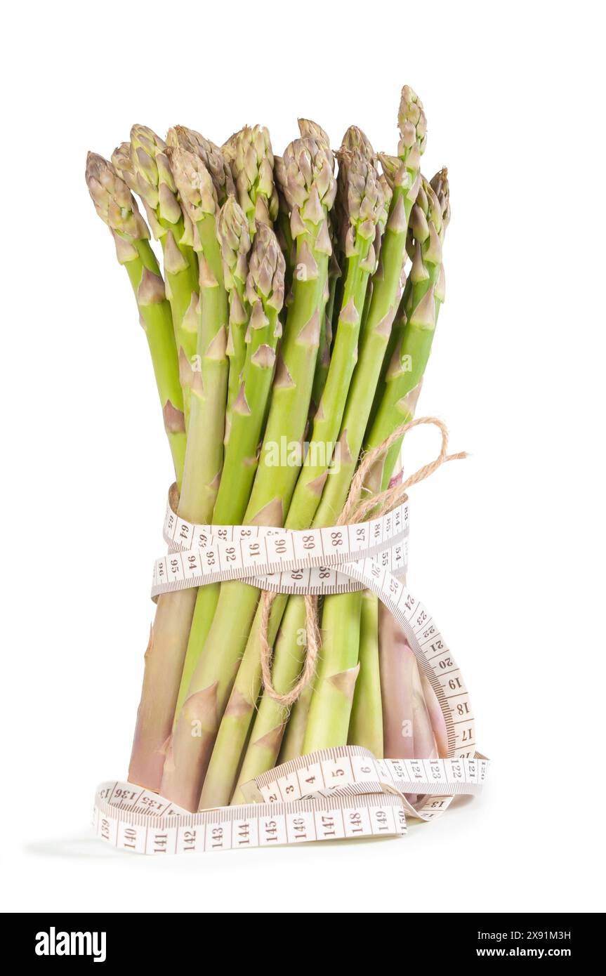 Un fascio di asparagi verdi freschi è ben avvolto con un metro a nastro, che simboleggia una sana alimentazione e una consapevolezza nutrizionale. spe verde brillante Foto Stock
