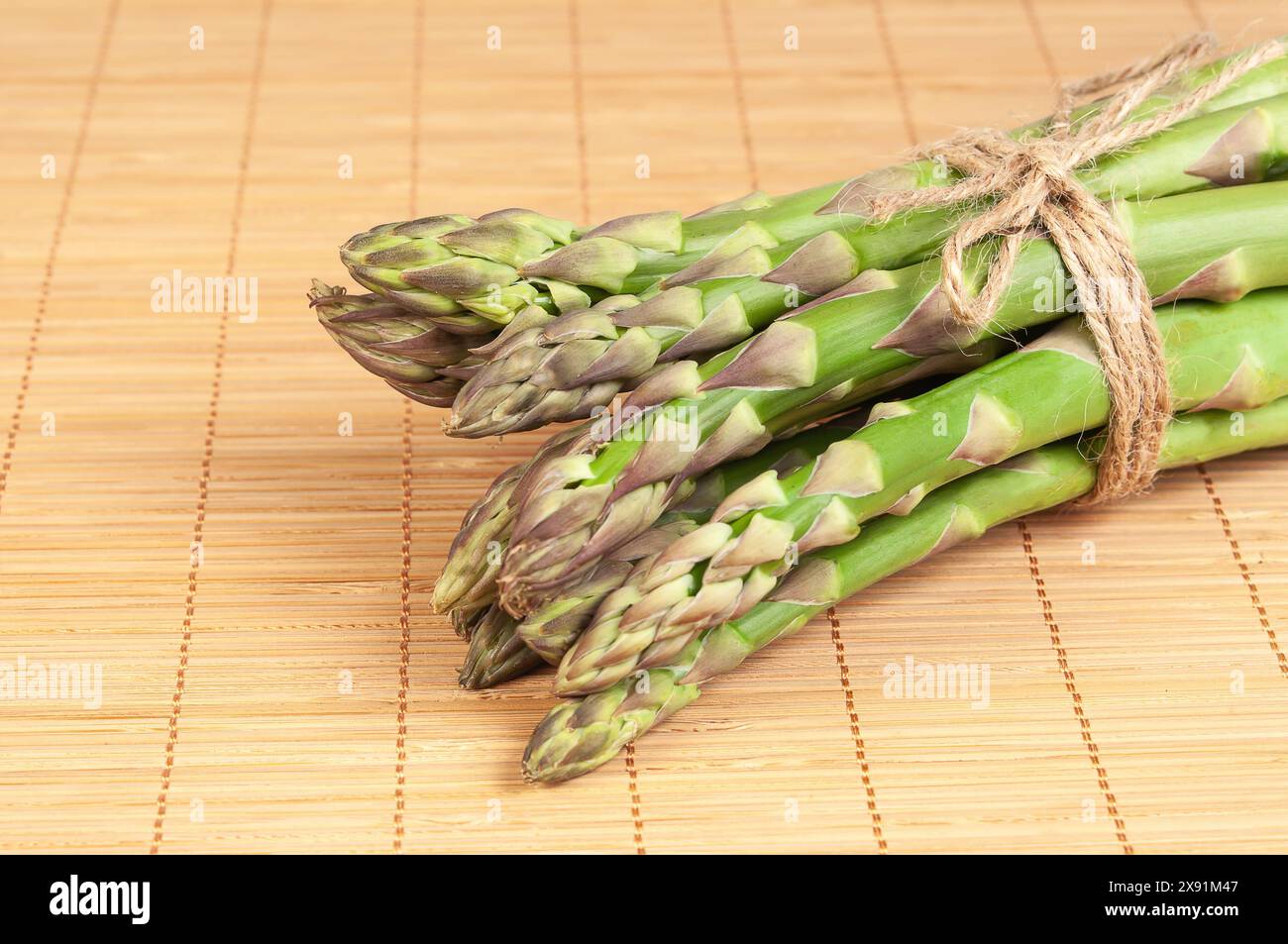Lancette di asparagi verdi fresche disposte in modo ordinato su un tappeto di bambù, con illuminazione naturale che mette in risalto il vibrante colore verde. Foto Stock