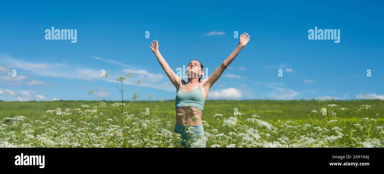 Donna sportiva con le braccia alzate per festeggiare e godersi il sole nel campo dei fiori selvatici Foto Stock