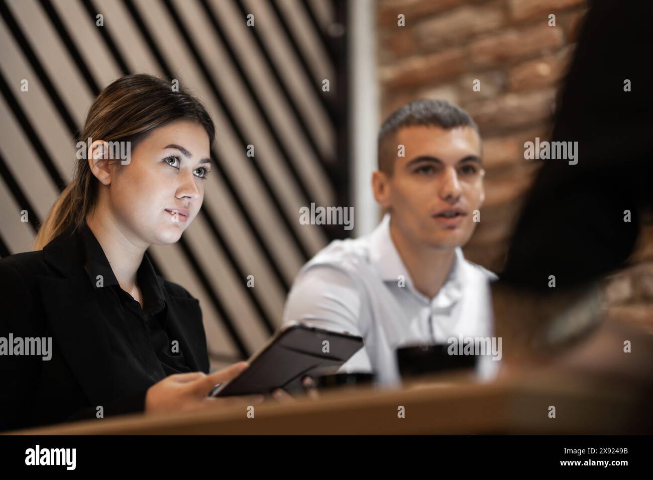 Una giovane donna e un uomo attenti partecipano a una riunione d'affari, mostrando professionalità e lavoro di squadra in un ufficio elegante. Foto Stock