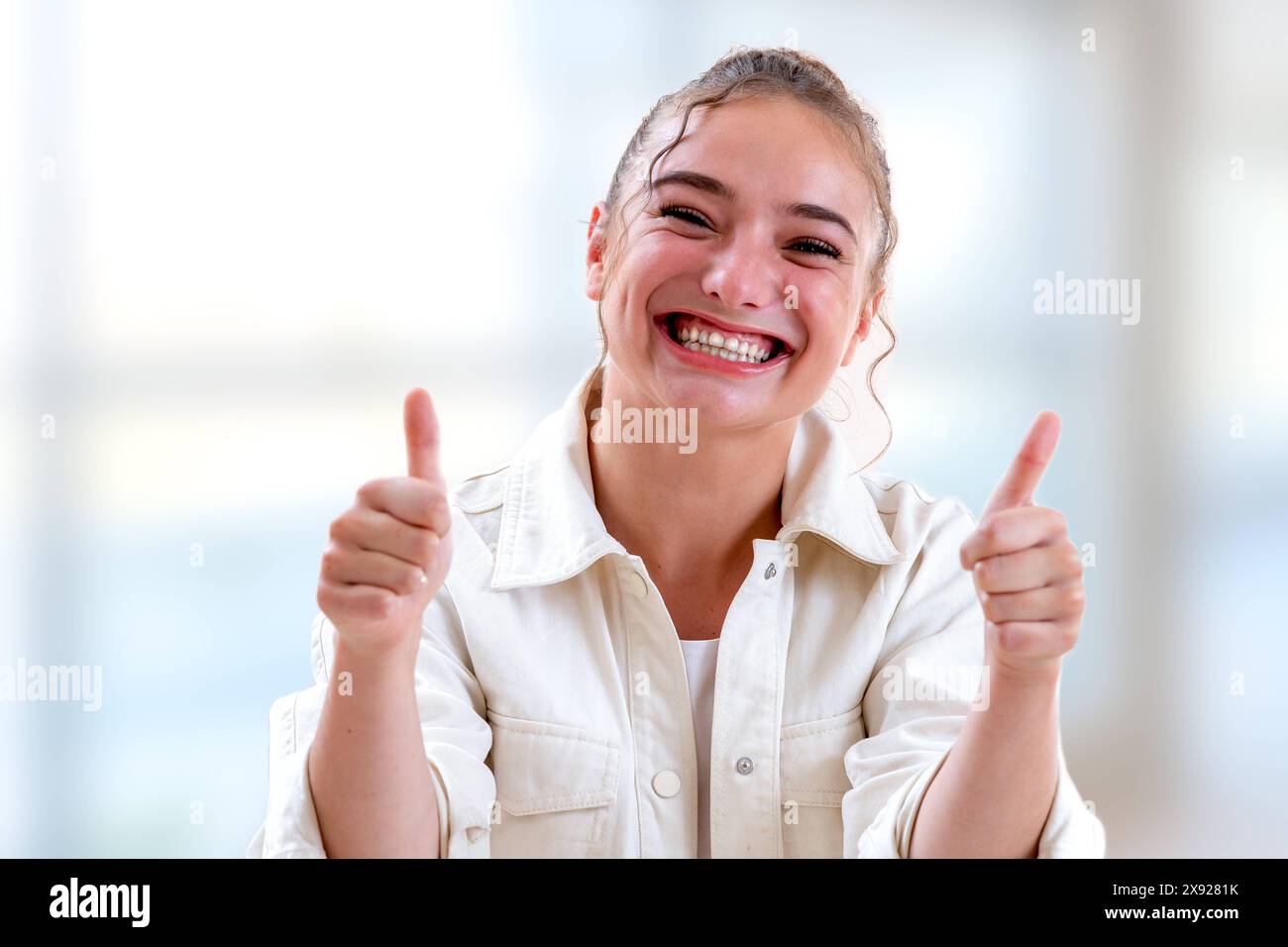 Foto orizzontale di una donna che esprime la sua gioia tenendo i pollici in alto la giovane donna che si fa ridere su uno sfondo luminoso e sfocato 016644 010 Foto Stock