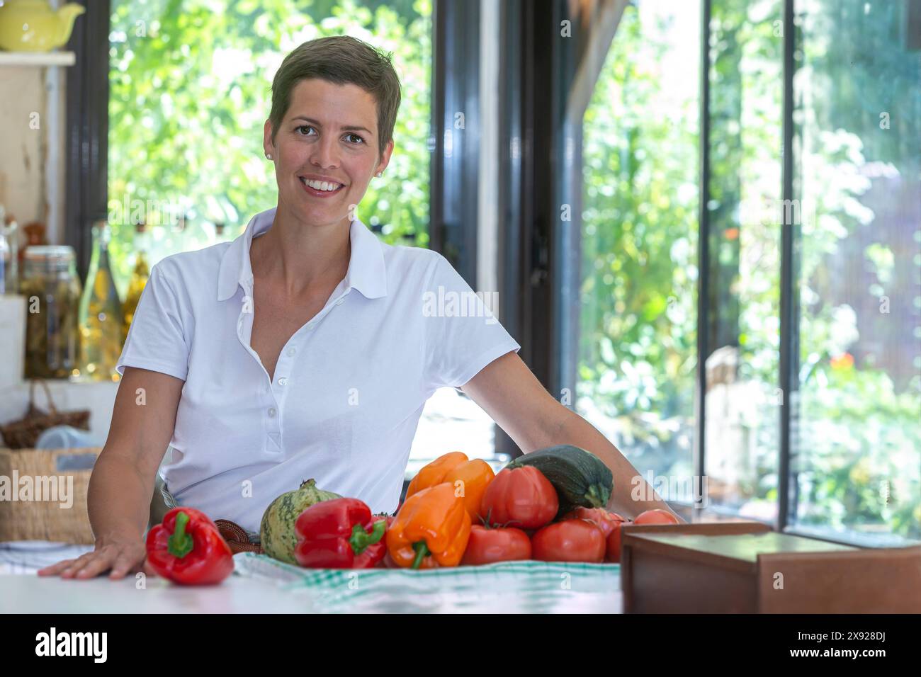 Donna bruna sorridente con capelli corti e un mucchio di verdure biologiche davanti a lei. Ritratto di una giovane donna in cucina 016643 094 Foto Stock