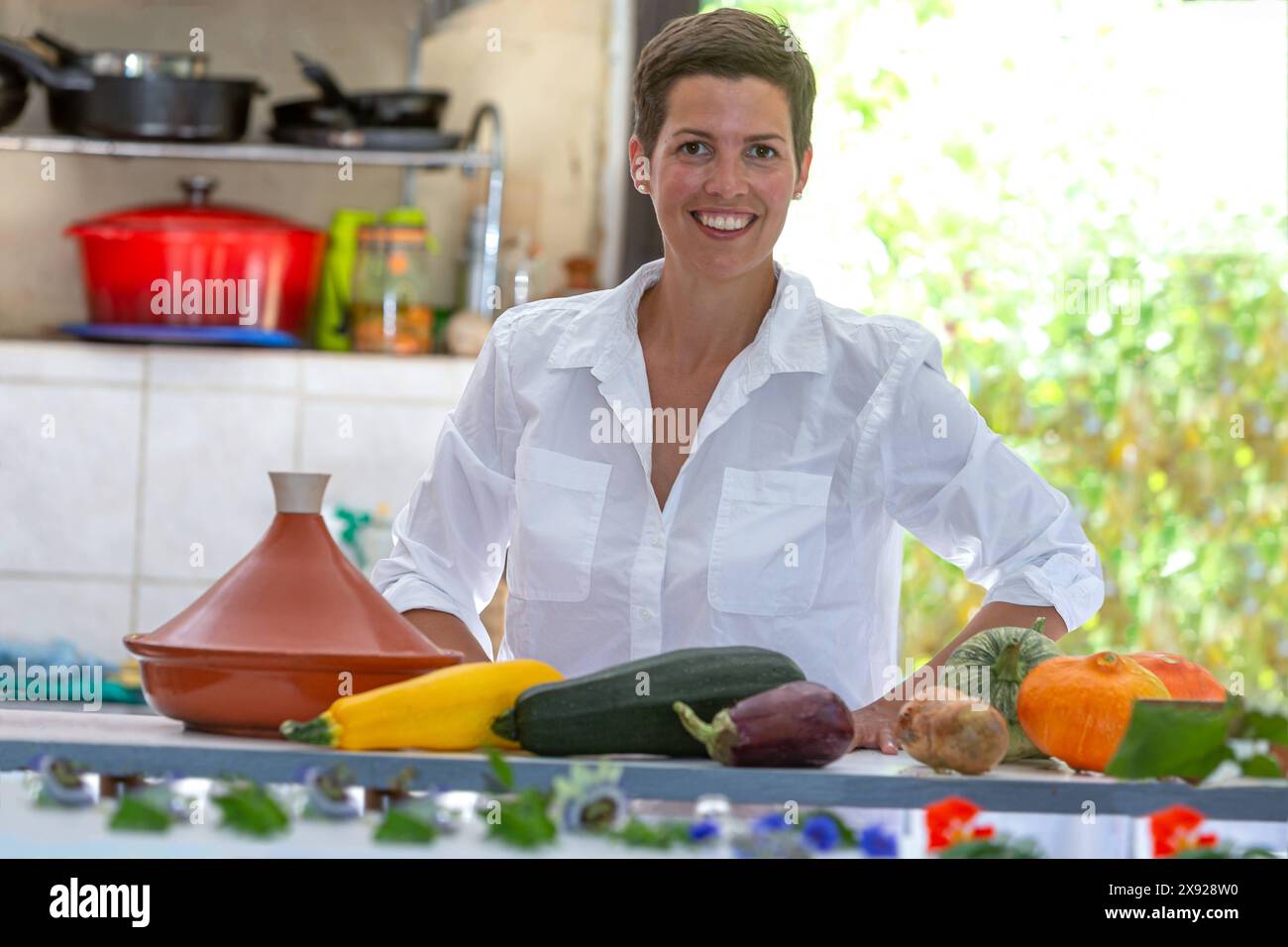 Giovane donna sorridente dietro un piano di lavoro che sostiene le verdure dell'orto per il tagine. Ritratto di una donna nella sua cucina 016643 097 Foto Stock