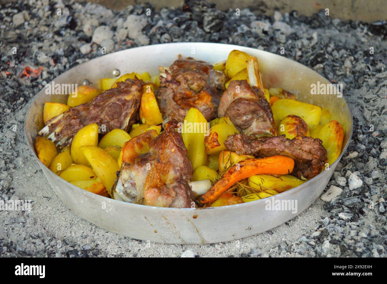 Cucina tradizionale croata. Carne arrosto, patate e carote preparate sotto un campanello di cottura, fuoco aperto con le braci. Foto Stock