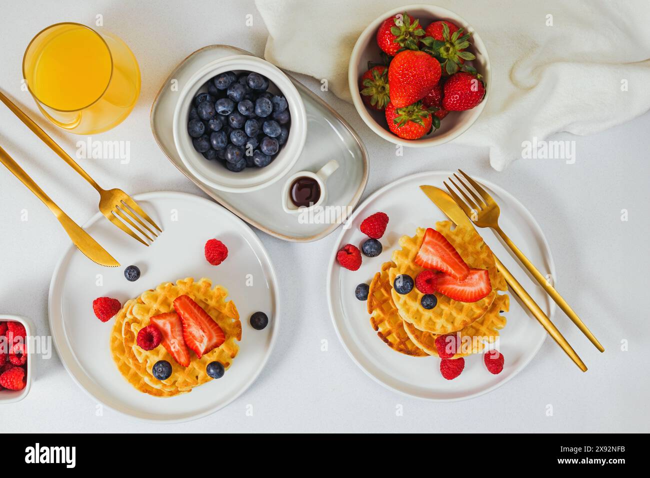 Waffle dolci fatti in casa serviti con diversi frutti di bosco e sciroppo d'acero, deliziosa colazione o brunch sul tavolo bianco, vista dall'alto Foto Stock