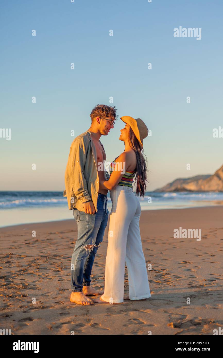 Vertical Un momento romantico immortalato da una coppia ispanica multiculturale che guarda affettuosamente negli occhi l'un l'altro sulla spiaggia durante un bellissimo summ Foto Stock