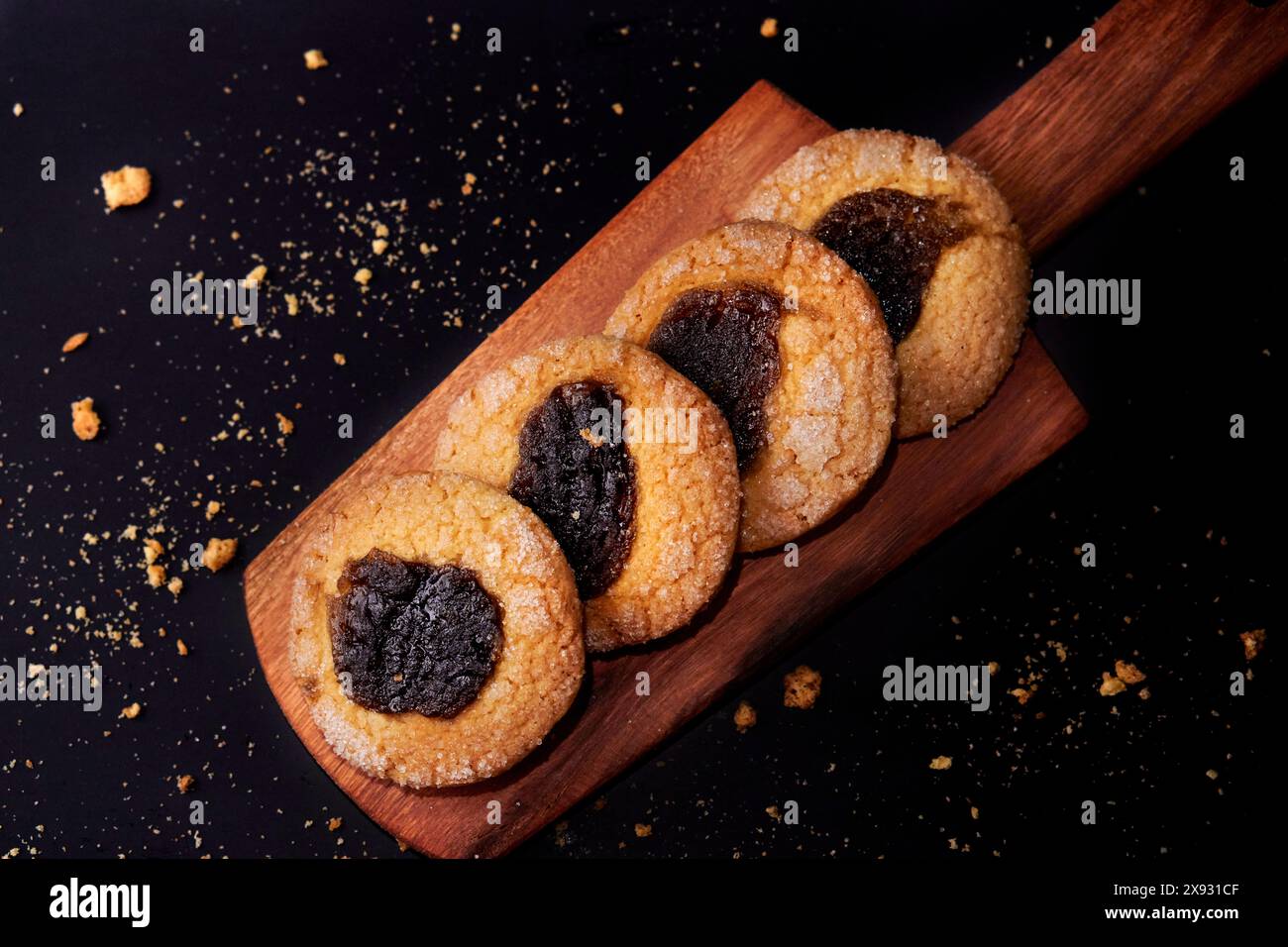 Fila di biscotti dolci rotondi con marmellata di cotogna in prospettiva su un asse di legno su sfondo nero Foto Stock