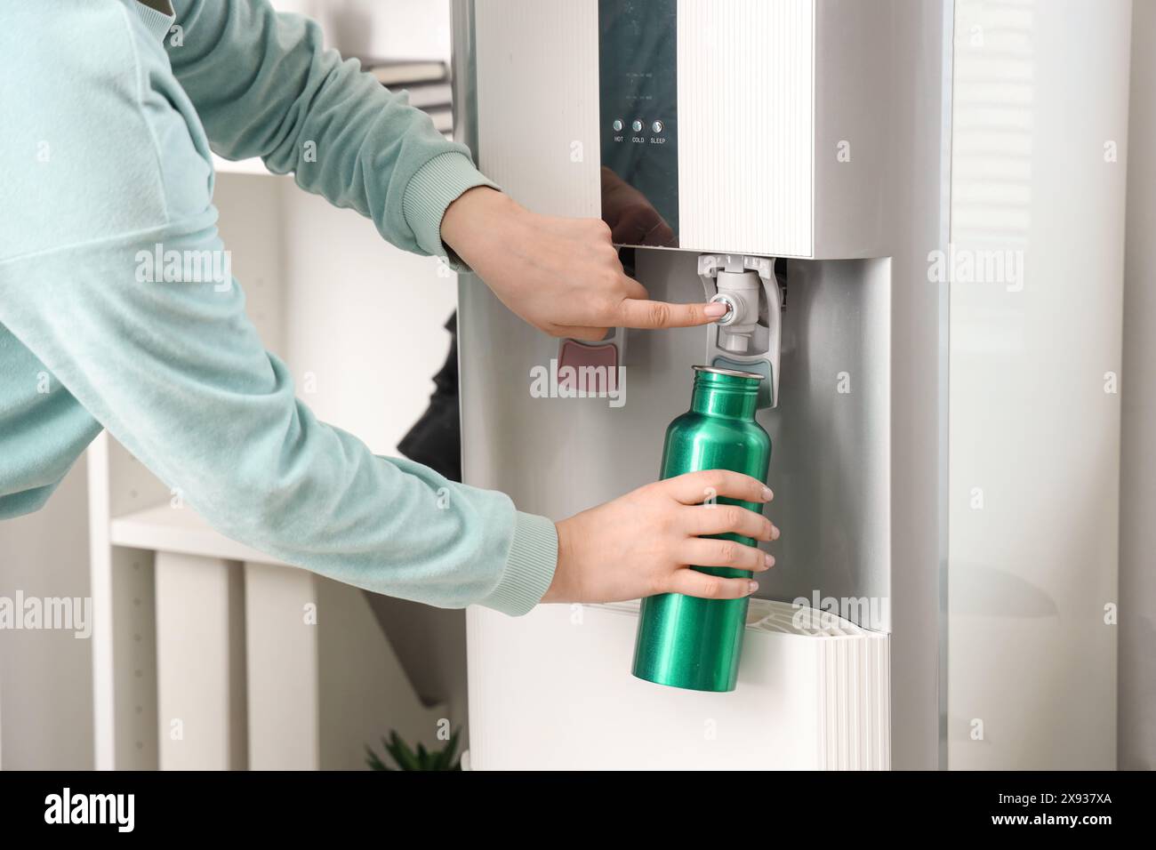 Bottiglia di riempimento mani femminili con acqua filtrata dal refrigeratore in camera Foto Stock