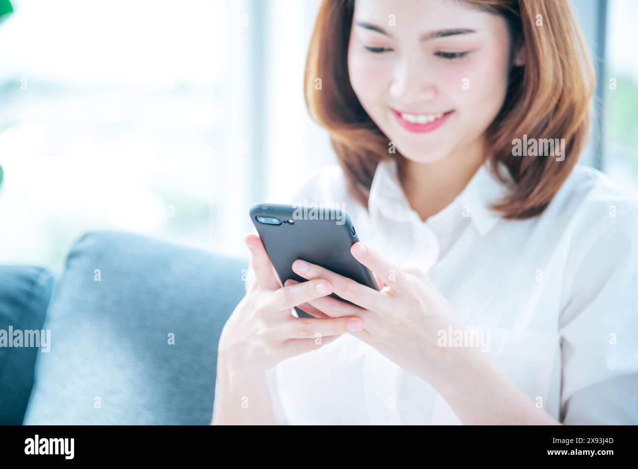 Donna asiatica che usa lo smartphone che legge i social media online che fanno shopping online sito web su smartphone con la faccia del sorriso. Felicità donna asiatica che tiene il cellfone Foto Stock