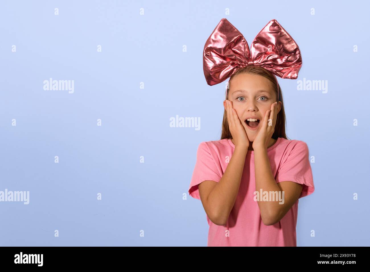 Una ragazza con un grande arco di carnevale sulla testa. Esprime gioia, piacere, sorpresa. Abiti per striscioni rosa, sfondo blu. Copia spazio Foto Stock