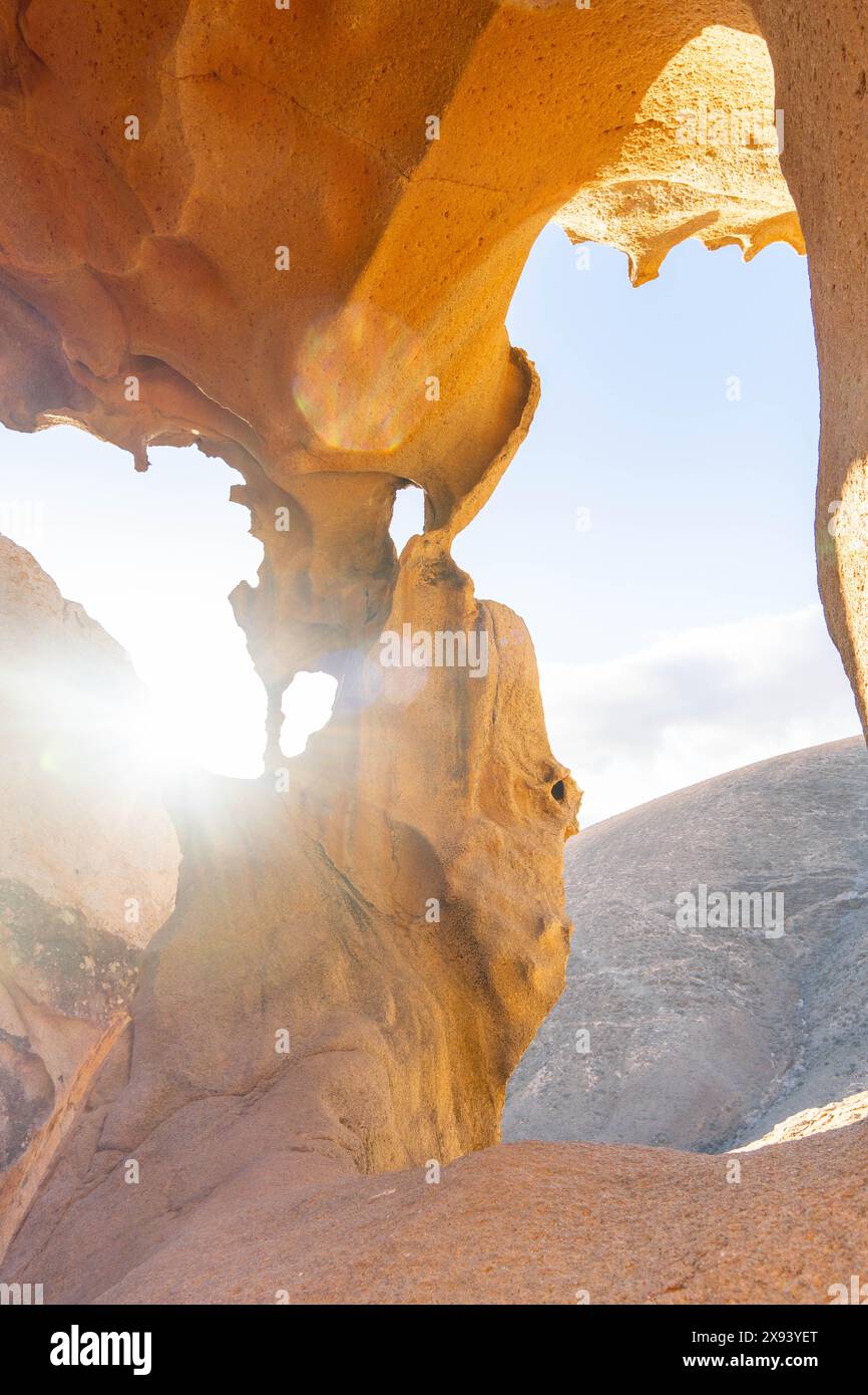 La luce del sole scorre attraverso le formazioni rocciose naturali dell'Arco de las Penitas, Fuerteventura, creando uno splendido gioco di luci e ombre su una limpida da Foto Stock