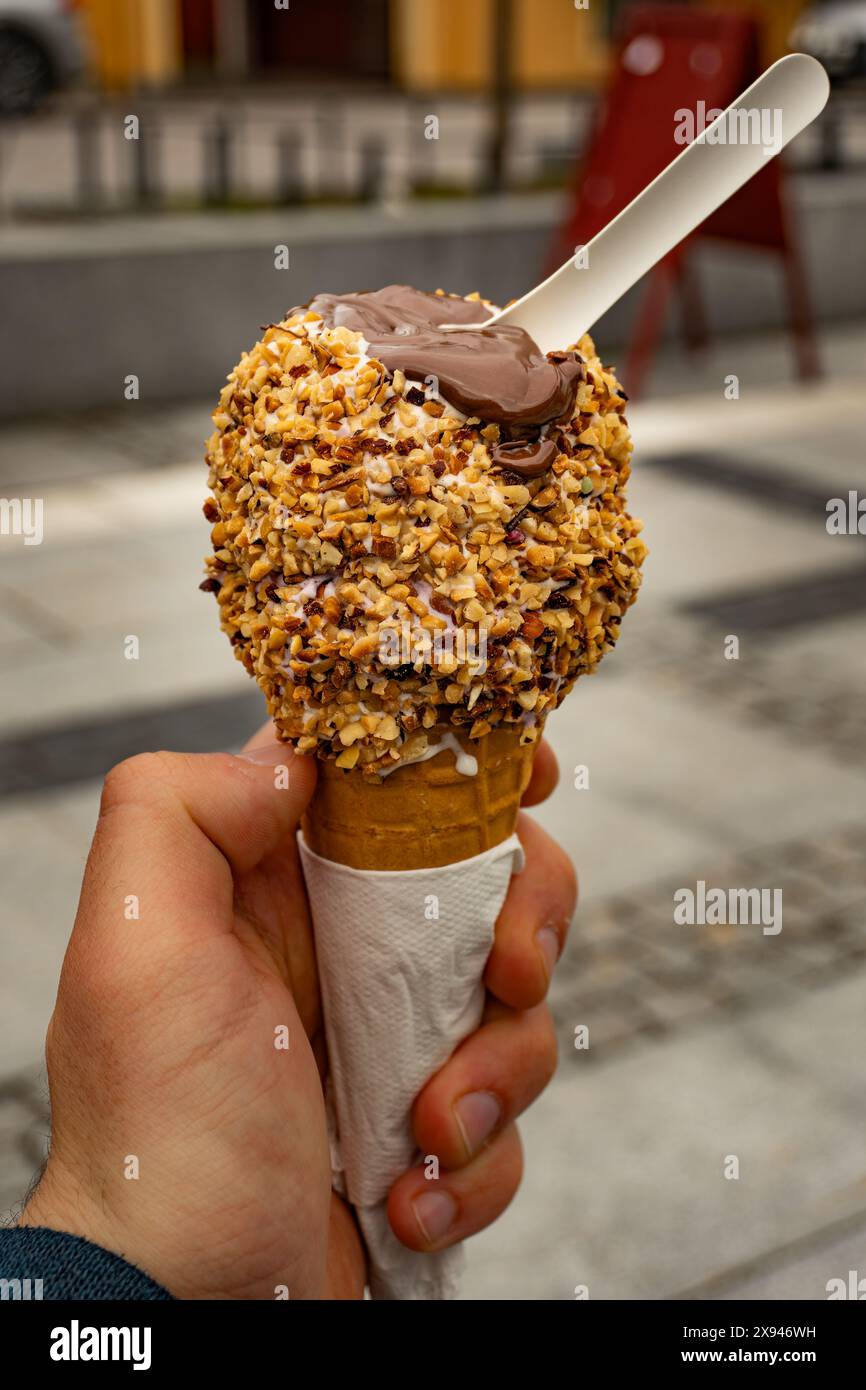 Tenendo a mano un cono gelato con uno sfondo panoramico del villaggio, catturando le semplici gioie della vita rurale. Foto Stock