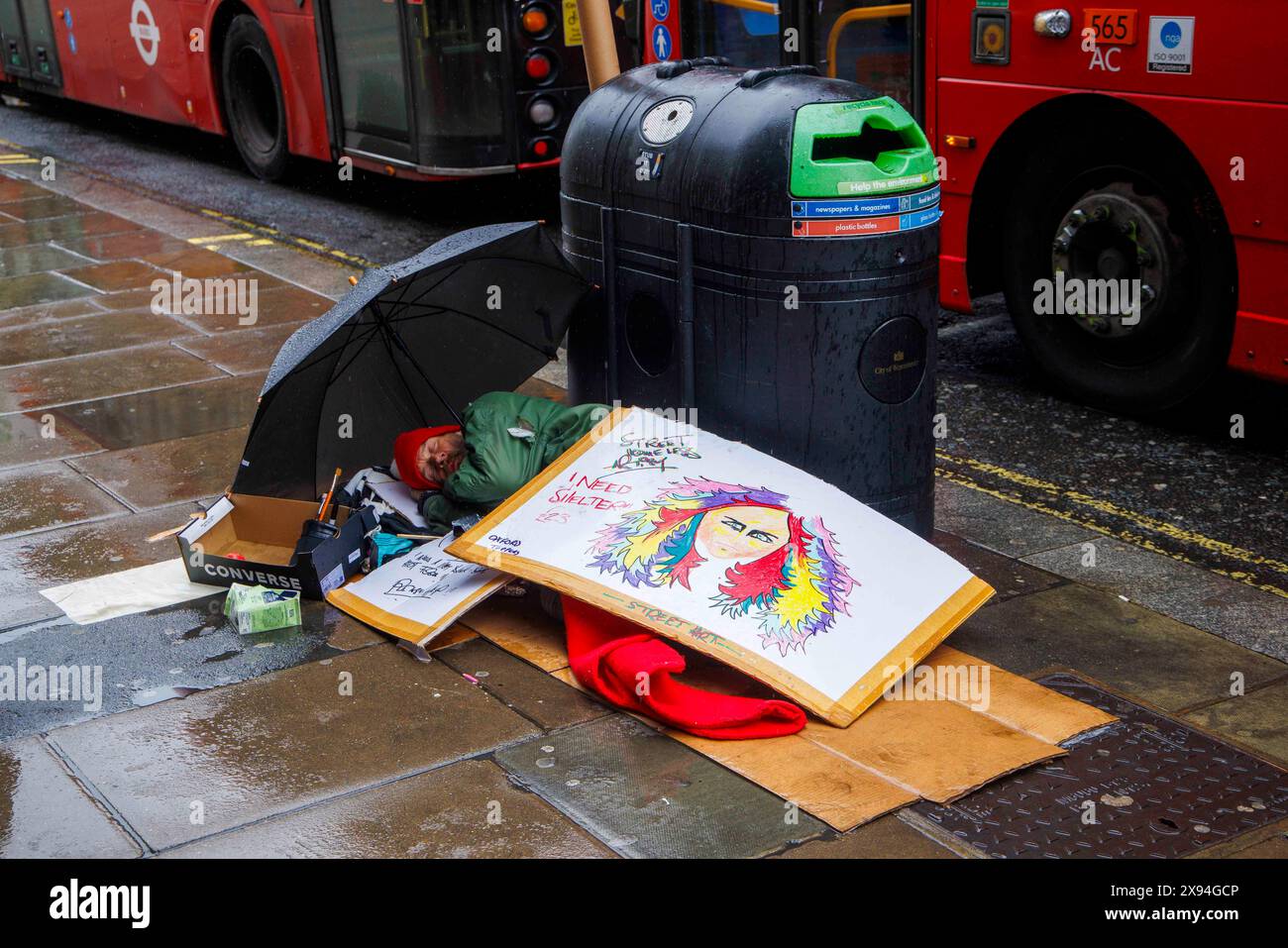 Un senzatetto sotto la pioggia a Oxford Street dorme e ha un cartello che dice che ho bisogno di un rifugio. Una persona su 50 a Londra è senzatetto. Foto Stock