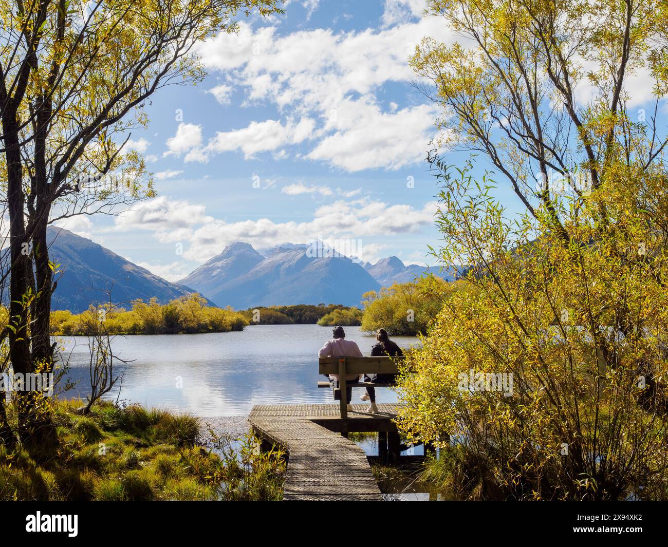 Coppia su una panchina che si affaccia sul Lago Wakatipu, sulla regione di Otago, sull'Isola del Sud, sulla nuova Zelanda, sul Pacifico Foto Stock
