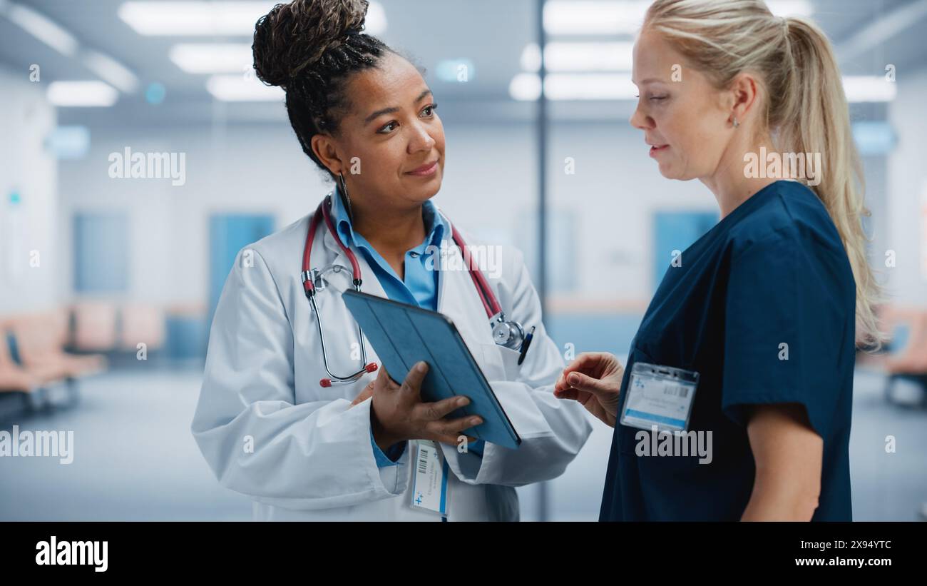 Ospedale medico: Medico femminile nero professionale parla con infermiera donna bianca utilizzando il computer digitale della compressa. Due specialisti sanitari discutono, trovare la soluzione di trattamento per salvare vite umane Foto Stock