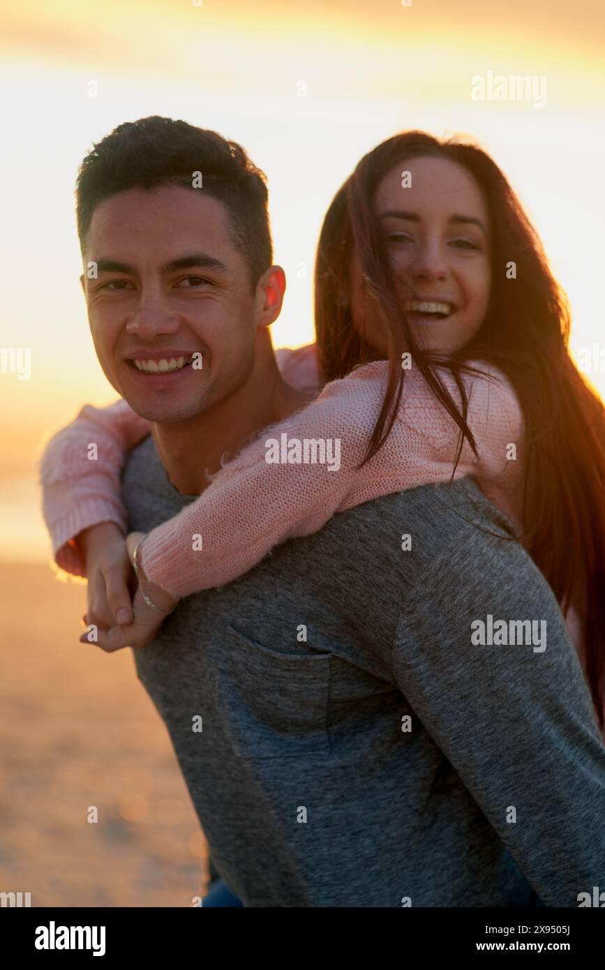 Felice, tramonto sulla spiaggia e ritratto di coppia con piggyback, divertimento e amore in riva al mare con cura. Abbracciate, abbracciate e legatevi con i giovani in vacanza con Foto Stock