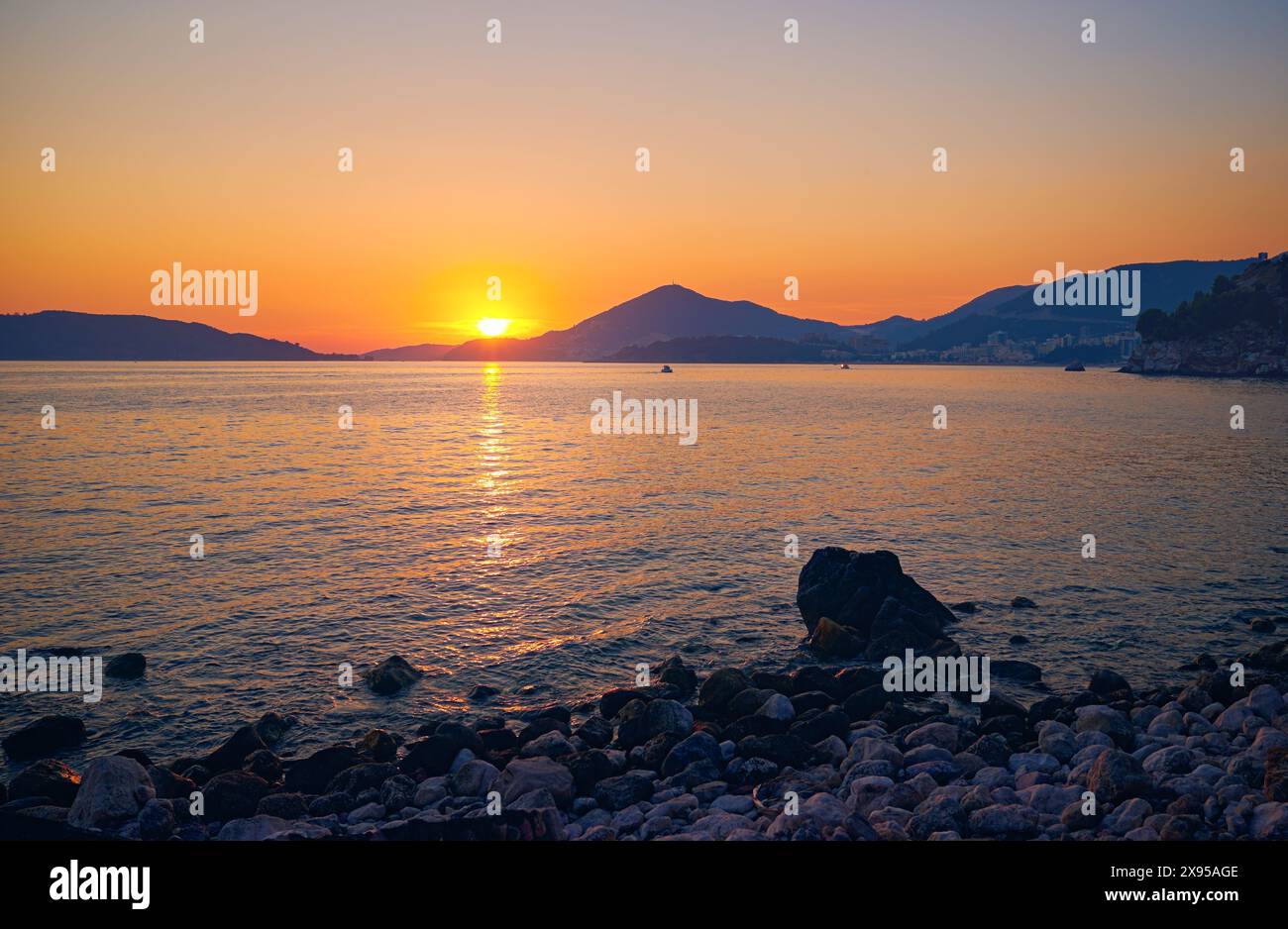 Il sole tramonta dietro le montagne sulla riva del mare in Montenegro Foto Stock