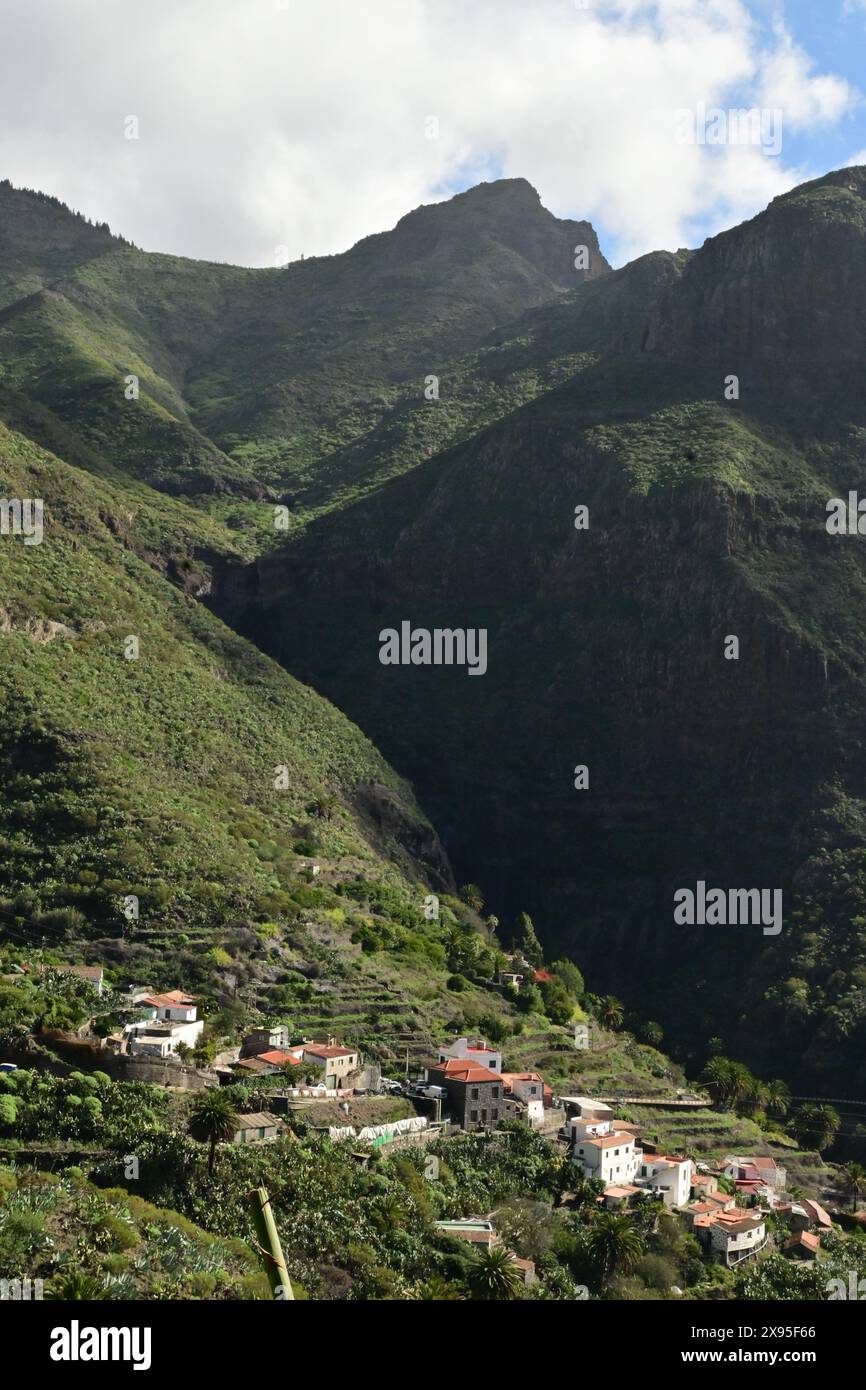 Tranquillo villaggio annidato tra lussureggianti montagne verdi con campi terrazzati, sotto un cielo parzialmente nuvoloso, catturando la tranquillità rurale Foto Stock