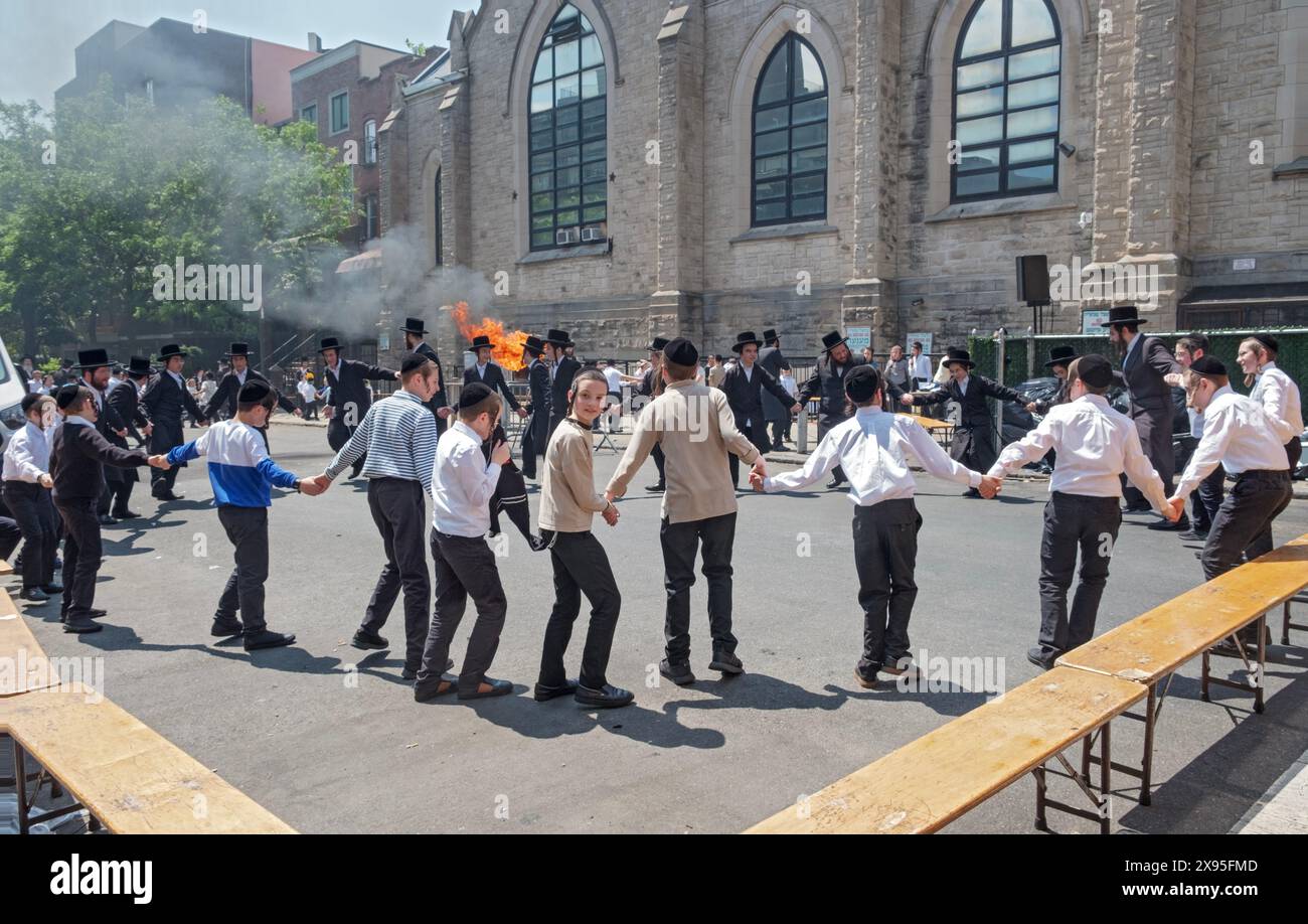 Gli studenti ebrei ortodossi celebrano il lag B'Omer ballando vicino a un fuoco tradizionale. In una strada chiusa a Brooklyn, New York. Foto Stock