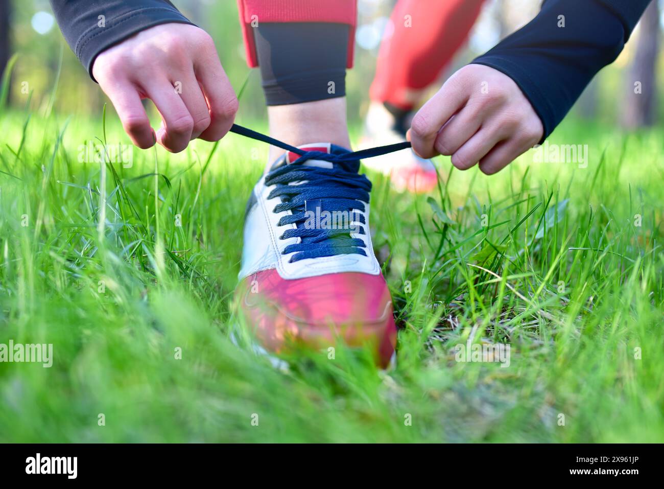 Persona che lega lacci scarpe a una sneaker rossa e bianca, preparandosi per un'attività all'aperto in un'area erbosa. Foto Stock