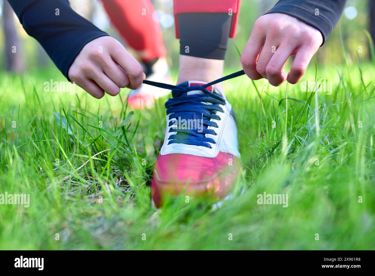 Persona che lega lacci scarpe a una sneaker rossa e bianca, preparandosi per un'attività all'aperto in un'area erbosa. Foto Stock