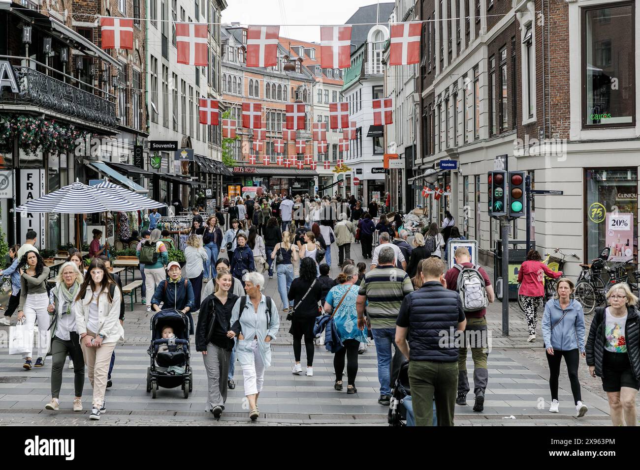 Copenaghen, Danimarca. 24 maggio 2024. La gente cammina in una strada nel centro di Copenaghen, con bandiere danesi appese sopra. Copenhagen si posiziona al quarto posto al mondo nel sondaggio sulla qualità della vita Mercer 2023. Un'economia stabile, eccellenti servizi educativi e un'elevata sicurezza sociale lo rendono attraente per la gente del posto e per i turisti. Copenaghen è anche una delle città più costose del mondo e una popolare destinazione turistica. Credito: SOPA Images Limited/Alamy Live News Foto Stock