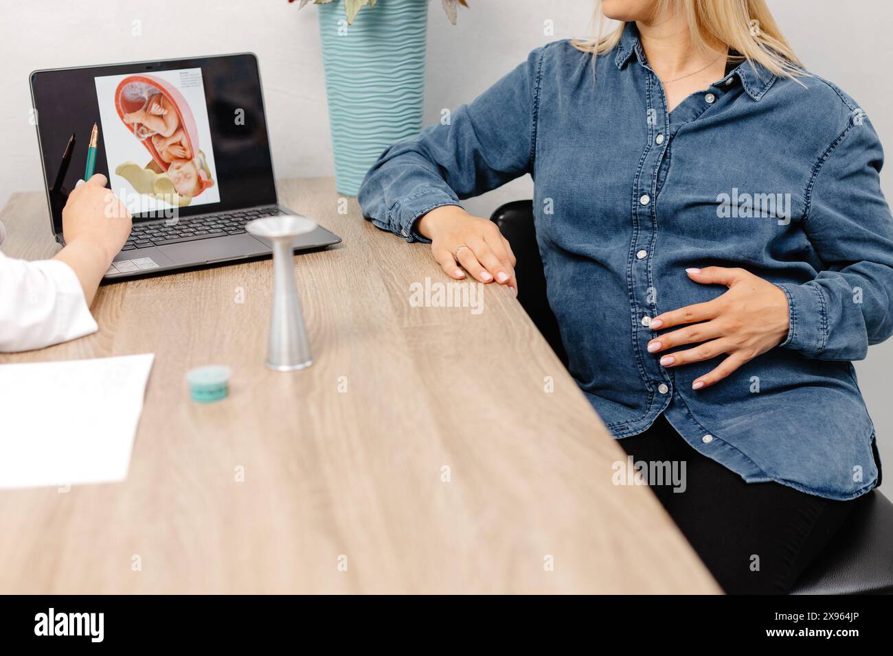 Giovane donna incinta che visita la sua ginecologa in clinica, seduta sulla sedia e parlando con il suo medico. Foto Stock