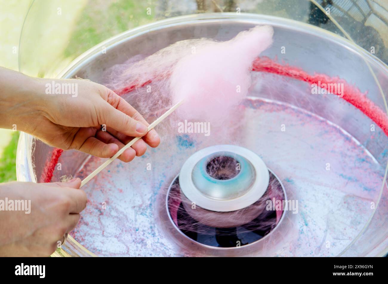 Vista ravvicinata della persona che filtra caramelle di cotone rosa con la macchina. Fai un giro all'aperto con il bastoncino di legno in estate. Foto Stock