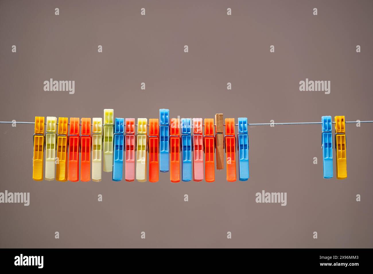 Una fila di pioli di plastica dai colori vivaci, pioli per lavanderia o clothespins su una linea di lavaggio. L'immagine viene scattata su uno sfondo semplice. Foto Stock