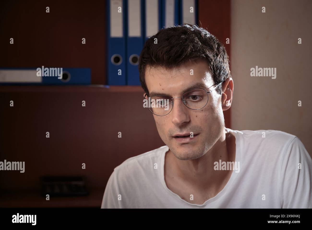 Ritratto di un giovane concentrato. La foto è stata scattata in ufficio e ci sono delle cartelle sullo sfondo. Primo piano. Foto Stock