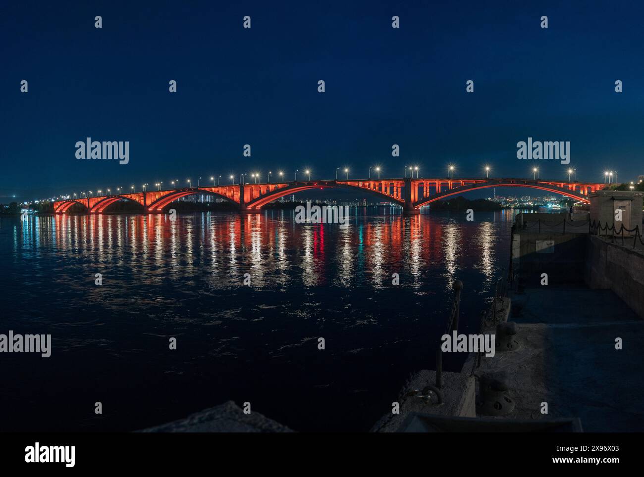 Un ponte che attraversa un corpo d'acqua durante la notte, adagiato su un paesaggio urbano con il cielo e l'orizzonte visibili sullo sfondo Foto Stock