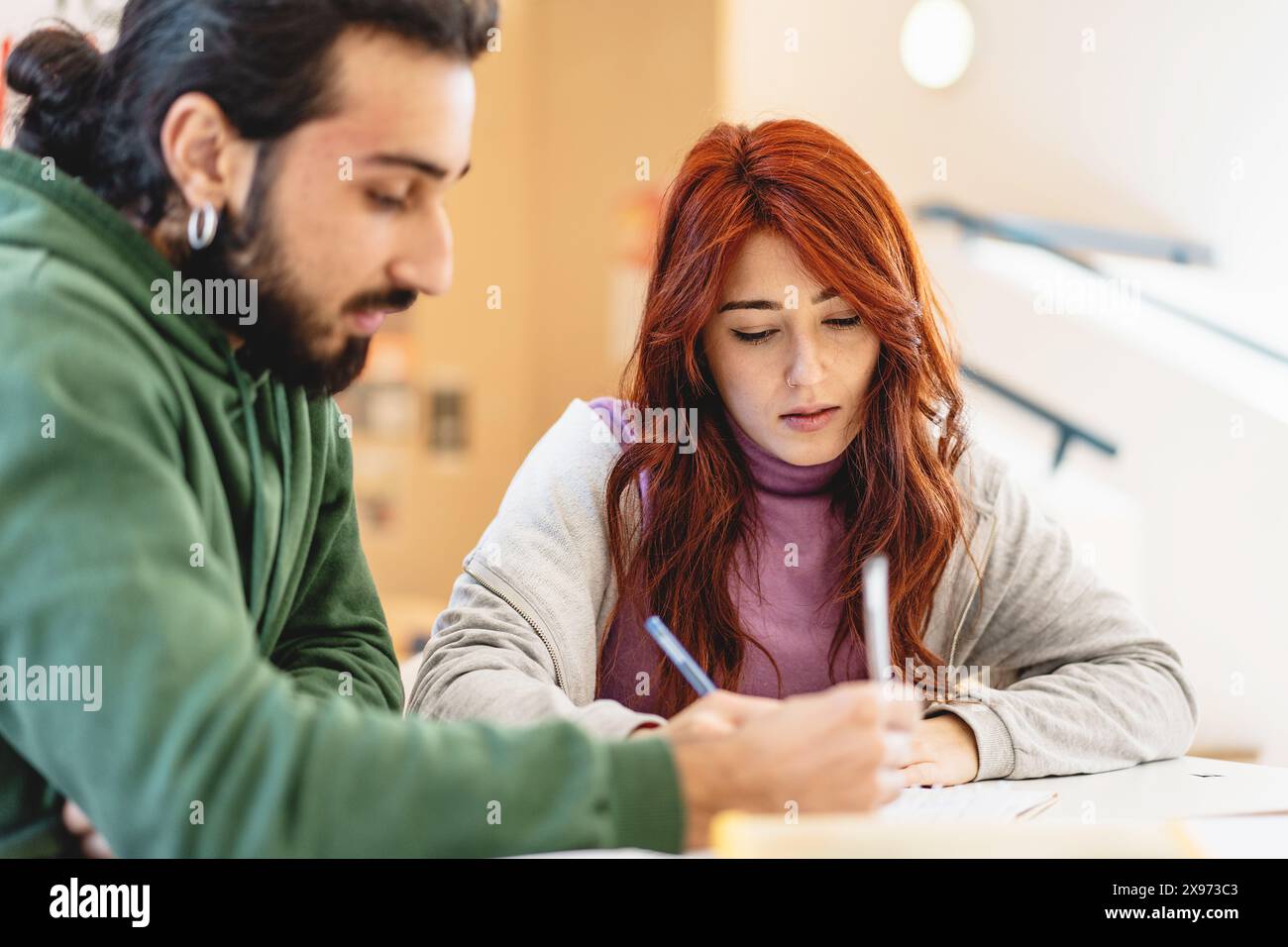 Due studenti focalizzati che scrivono appunti insieme in un ambiente di classe, studio collaborativo, apprendimento di giovani adulti, lavoro di squadra accademico, coinvolgimento e comprensione Foto Stock