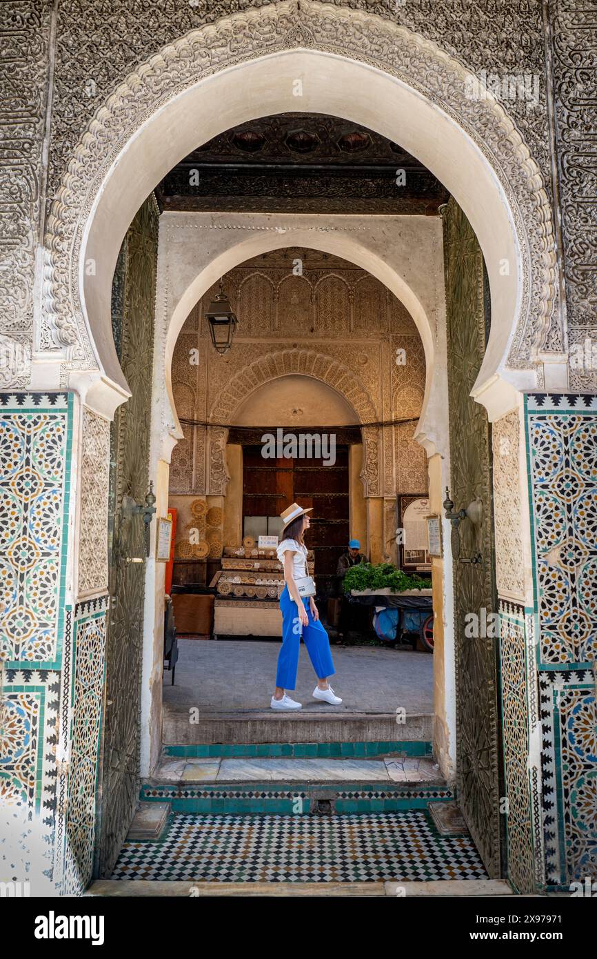 Young Woman che cammina attraverso Bou Inania Madrasa, uscita Archway, Fez, Marocco Foto Stock
