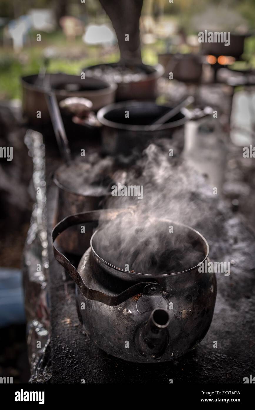 Cuocere a vapore la bevanda calda in una teiera con vecchie pentole di metallo in sottofondo cucinando all'esterno Foto Stock