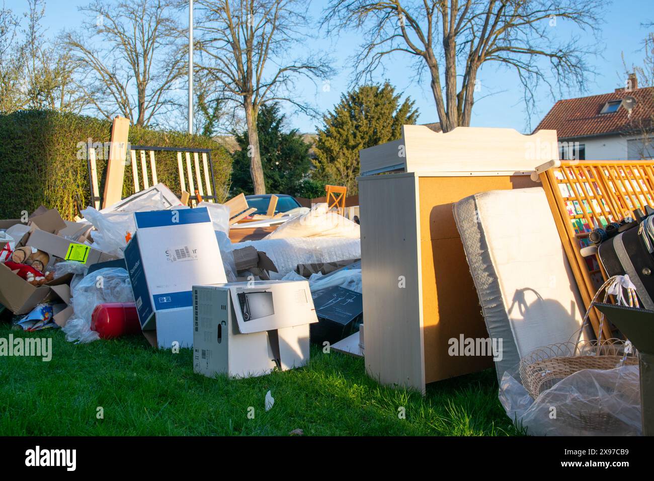 Un sacco di sprechi in una città vicino alla casa. Grande spazzatura con vecchi mobili in legno, giocattoli, scatole, sacchetti di plastica su una strada e erba verde in primavera soleggiata tra Foto Stock
