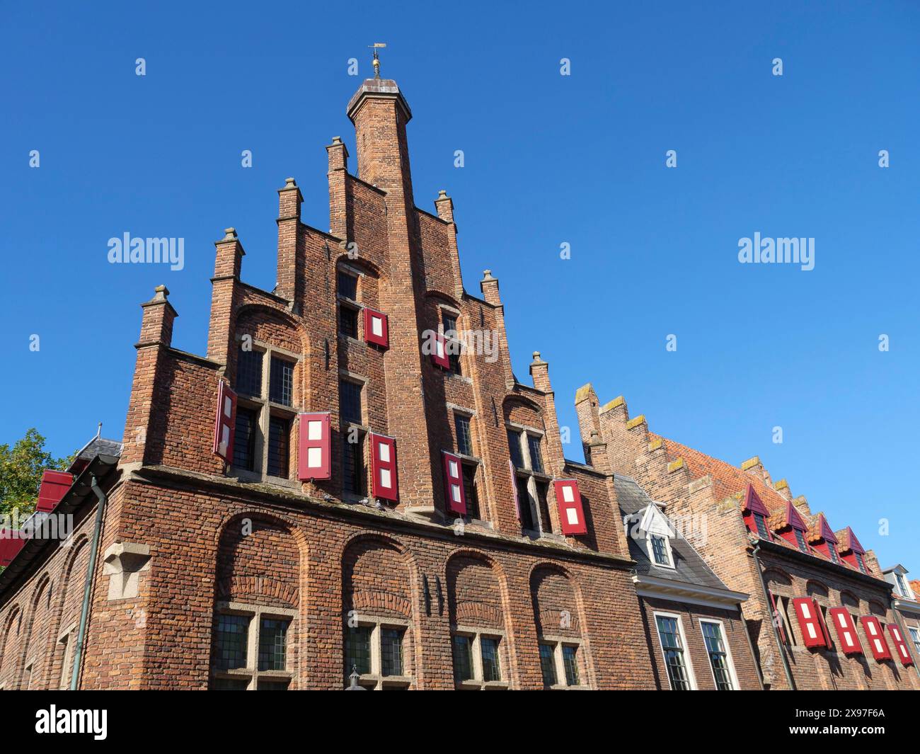 Edificio gotico con persiane rosse sotto un cielo azzurro, case in mattoni rossi e chiese nei Paesi Bassi, Doesburg, Paesi Bassi Foto Stock