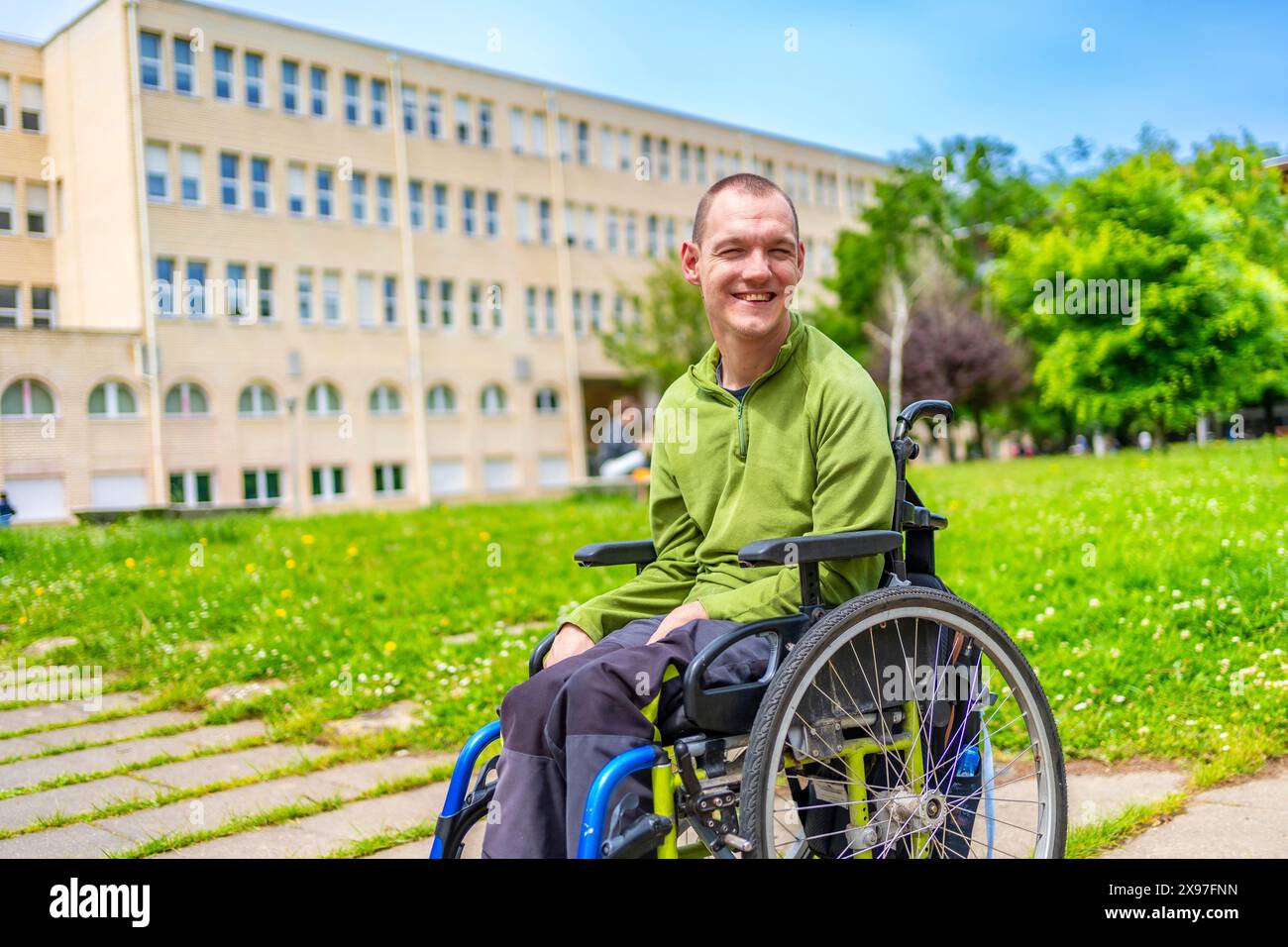 Uomo con disabilità seduto su una sedia a rotelle elettrica nel campus universitario Foto Stock