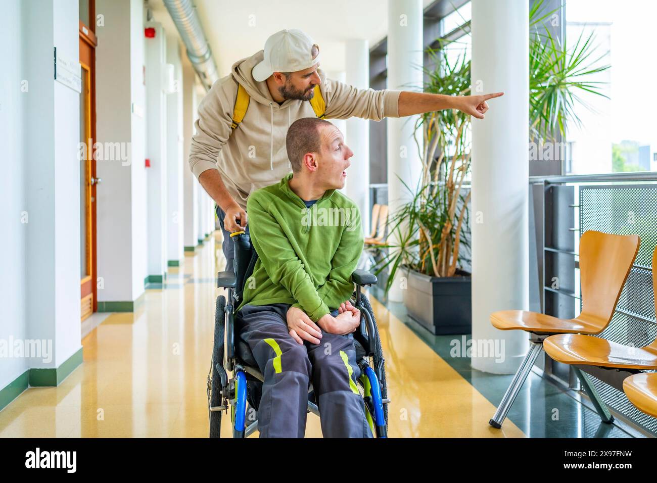 Giovane caucasico che mostra qualcosa fuori dall'università ad un amico disabile seduto su sedia a rotelle Foto Stock