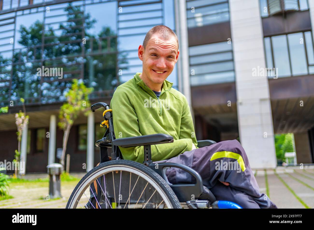 Uomo adulto caucasico con disabilità felice in sedia a rotelle sorridente alla macchina fotografica fuori dall'università Foto Stock