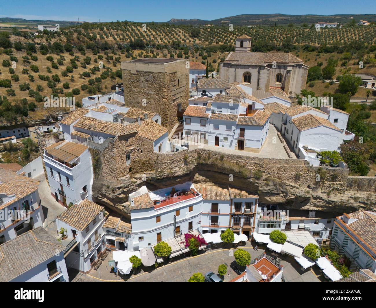 Villaggio spagnolo con edifici storici, chiesa e oliveti sotto un cielo soleggiato, circondato da un muro di pietra, vista aerea, abitazioni nelle grotte, Setenil Foto Stock