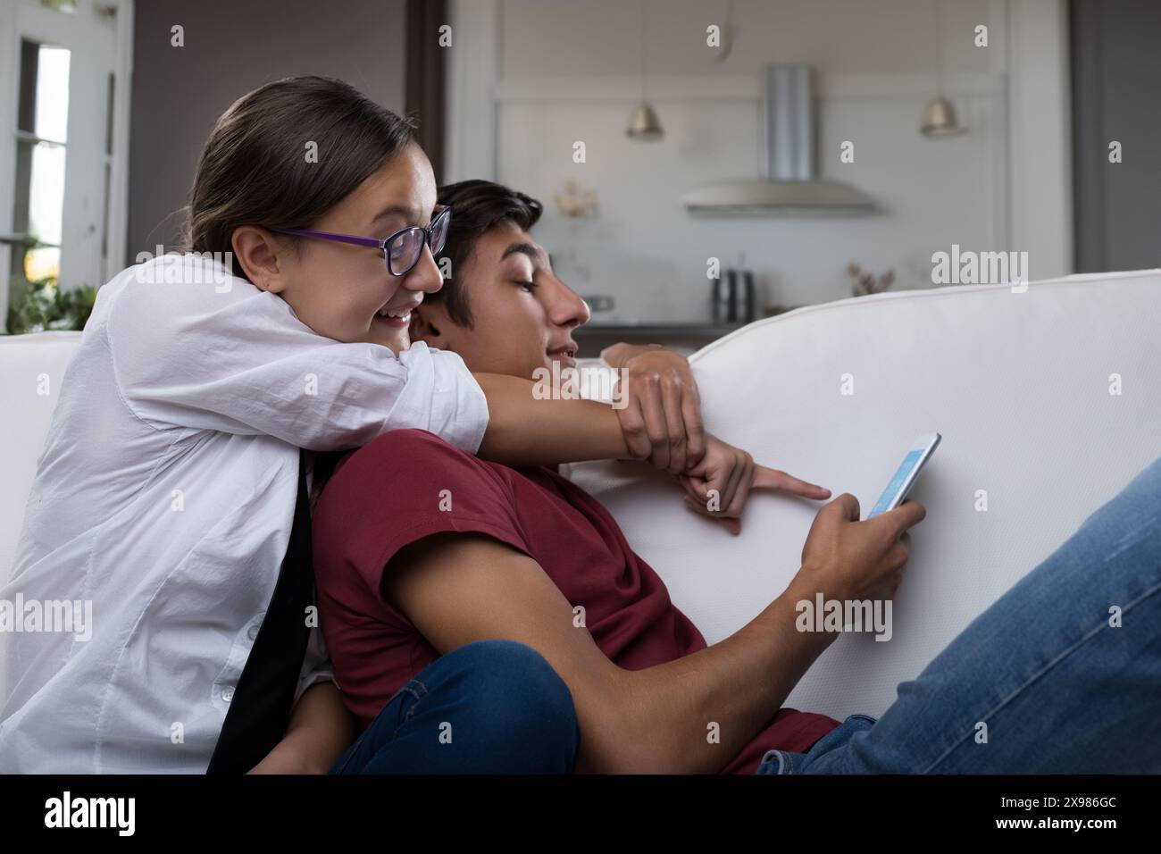 giovane donna, con occhiali e camicia bianca, punta allo smartphone del giovane uomo. Sembra divertito, suggerendo che stanno condividendo un divertente o intere Foto Stock