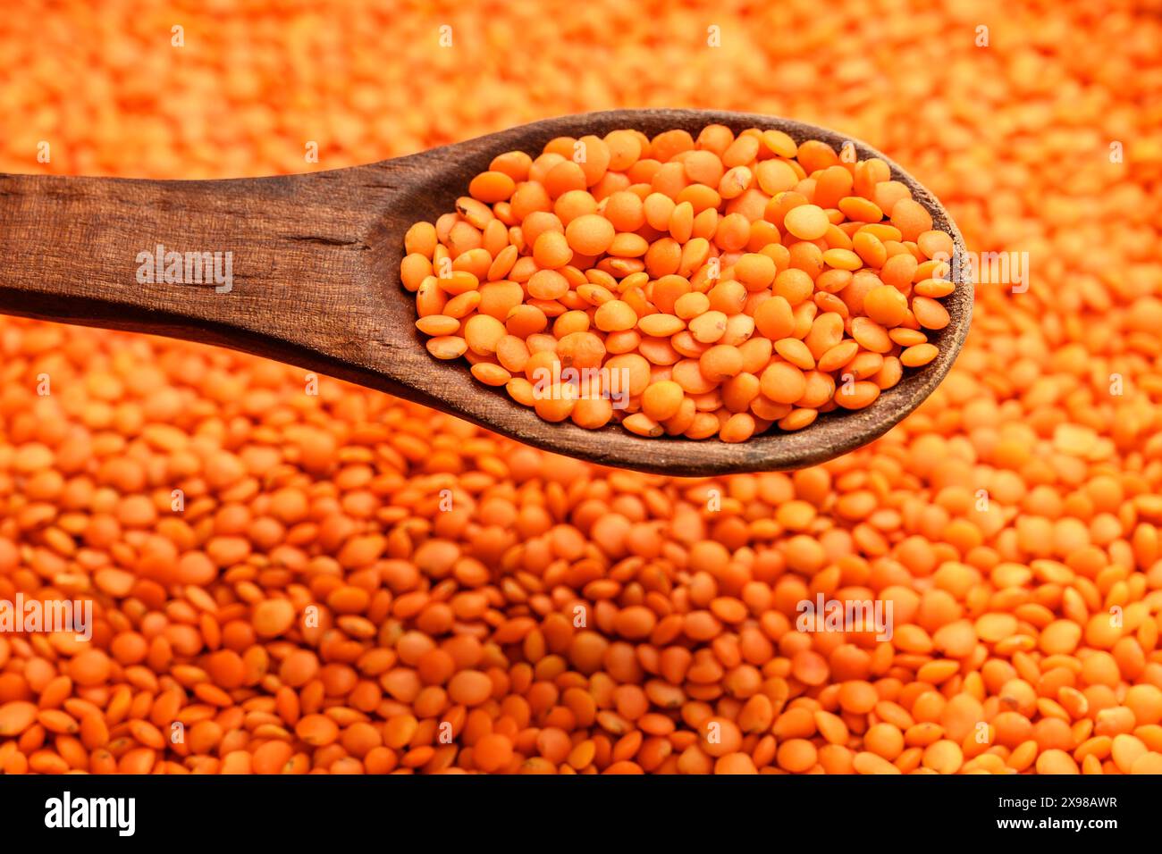 Lenticchie rosse che riempiono l'intero telaio e vengono sollevate da un cucchiaio di legno Foto Stock