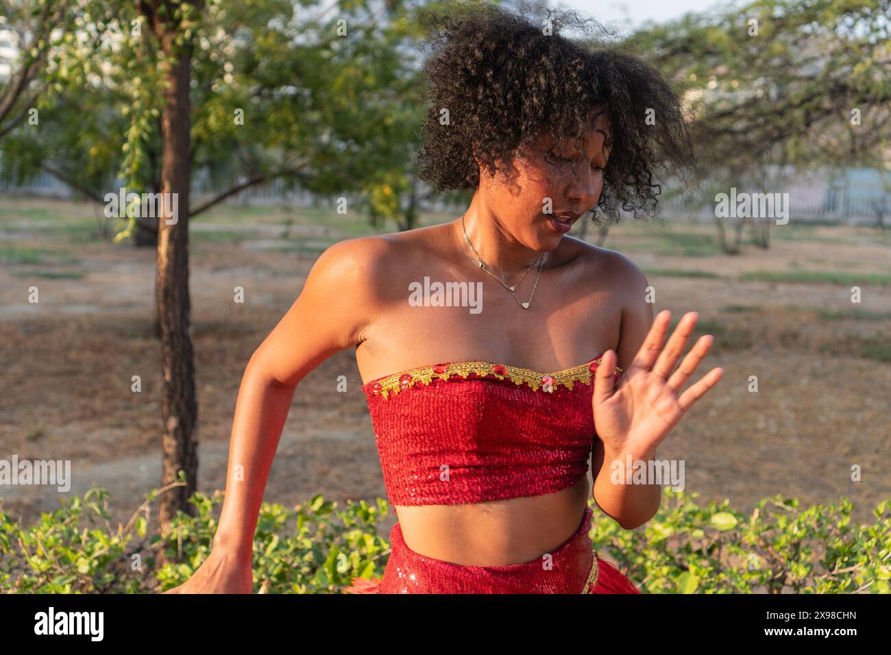 Donna in costume rosso che balla in un parco all'aperto, capelli ricci, movimento espressivo. Foto Stock