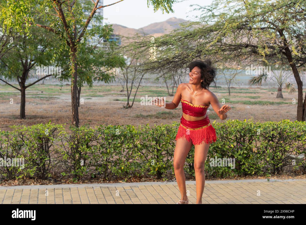 Allegra donna che balla in costume rosso all'aperto, capelli ricci, movimento espressivo. Foto Stock