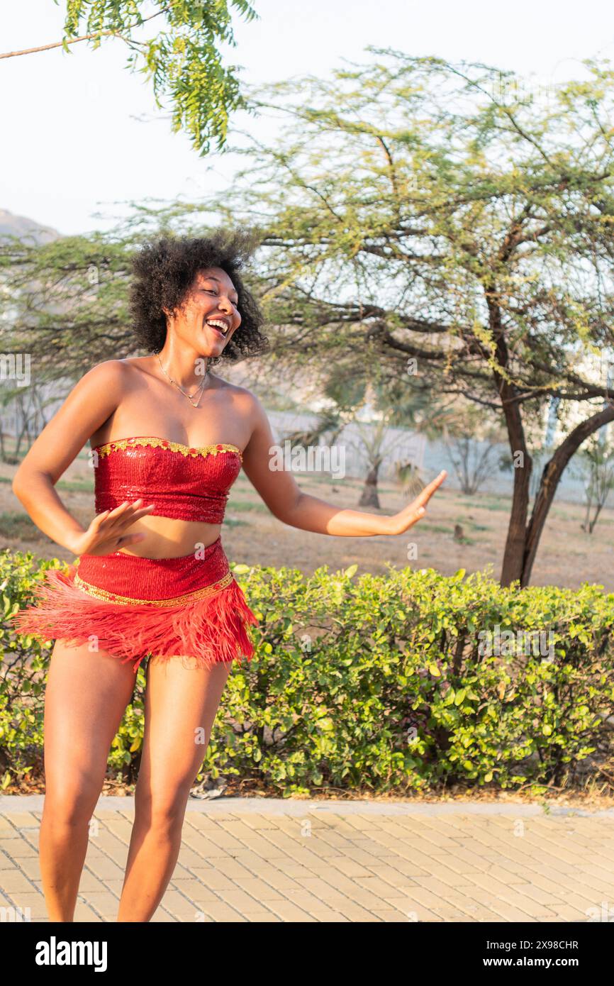 Donna felice che balla in costume rosso all'aperto, capelli ricci, movimento espressivo. Foto Stock