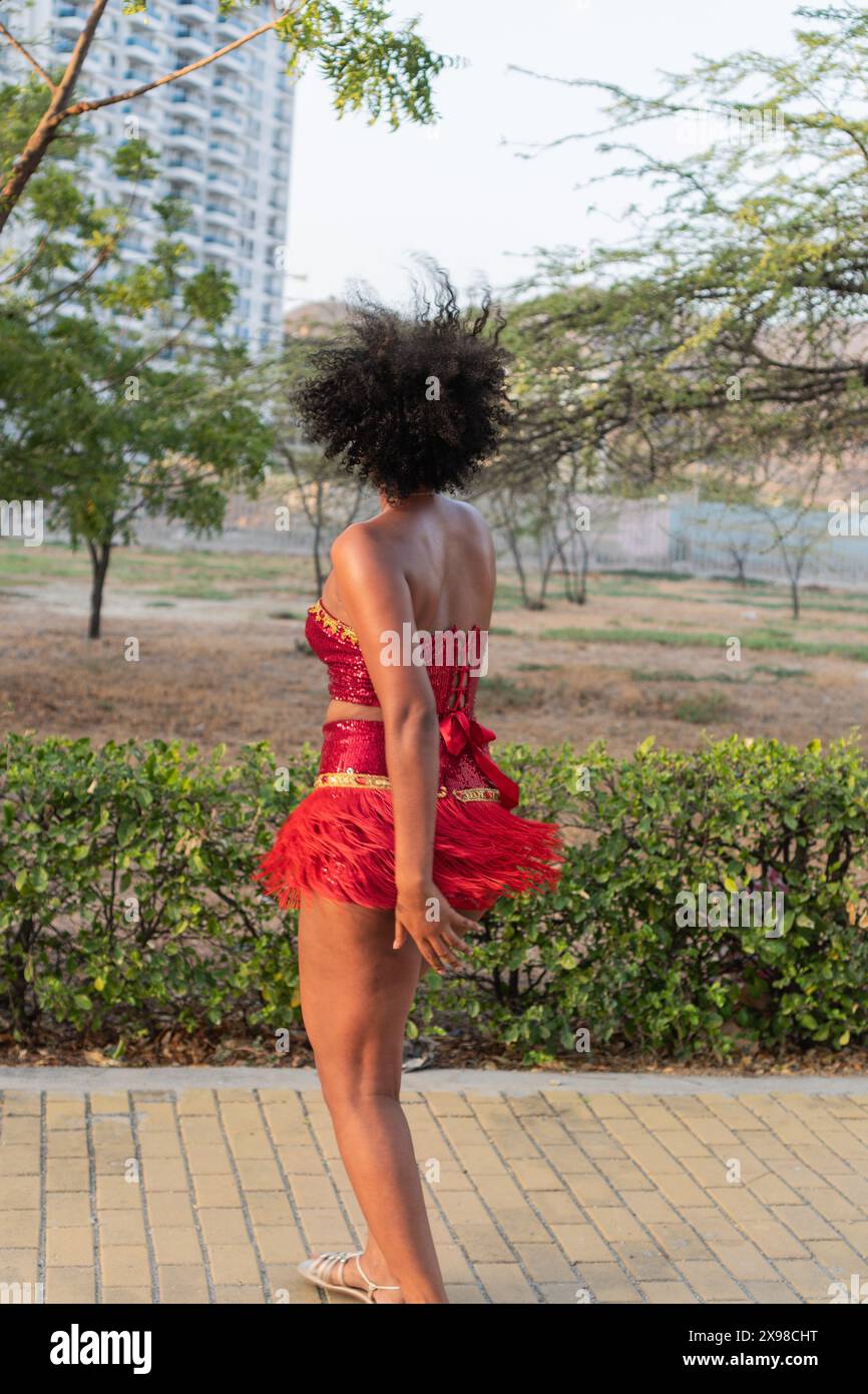 Donna in costume rosso che balla all'aperto, vista posteriore, capelli ricci, movimento espressivo. Foto Stock