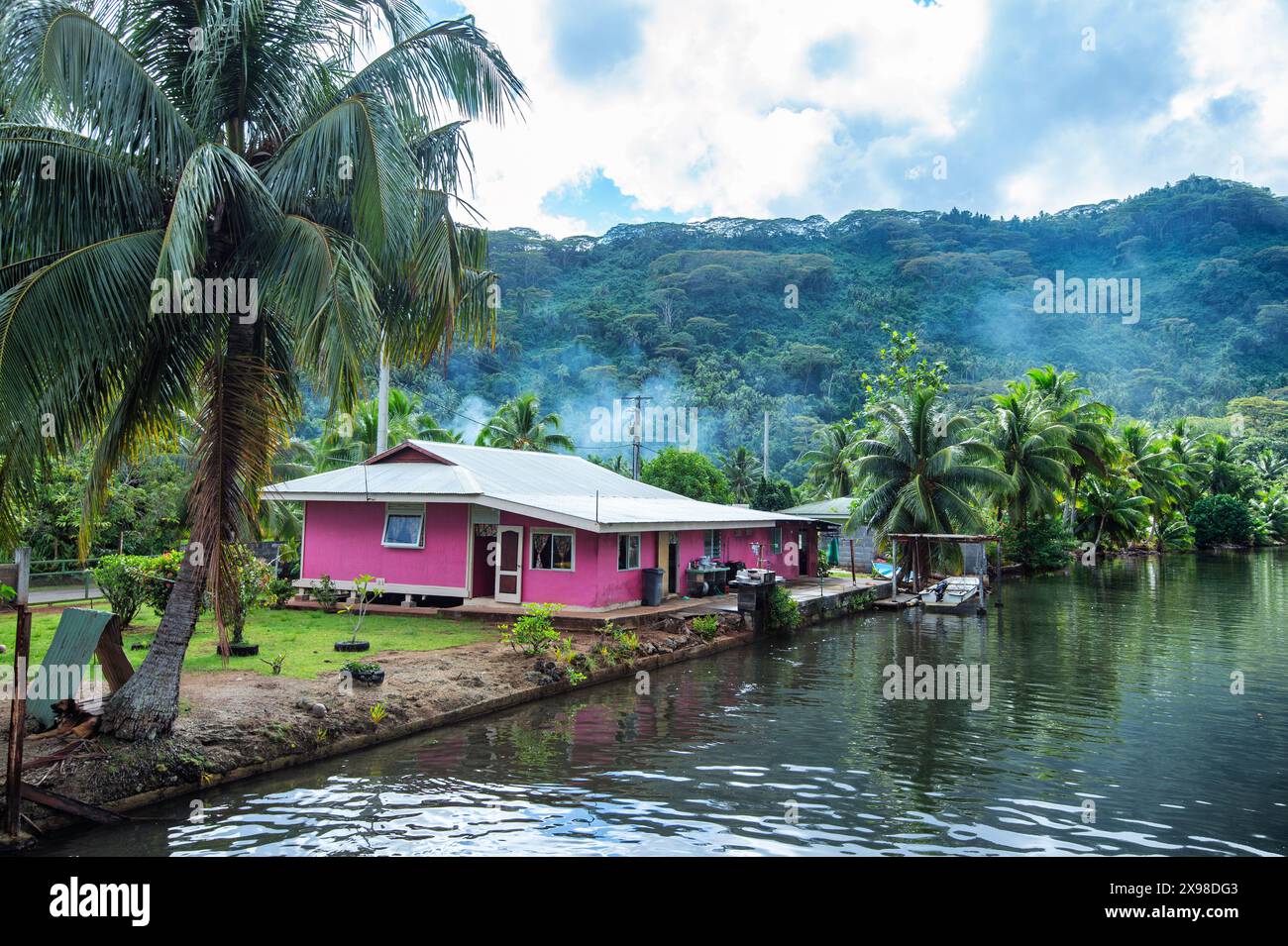 Graziosa e colorata casa rosa con palme lungo un fiume sull'isola di Taha'a, Polinesia francese Foto Stock