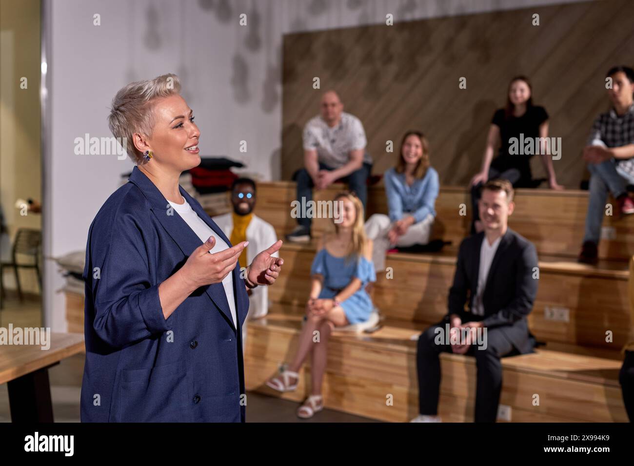 Docente femminile di abbigliamento formale sorridente, tenendo conferenze a gruppi di persone sullo sfondo, le persone si sono riunite per ascoltarla parlare di me Foto Stock