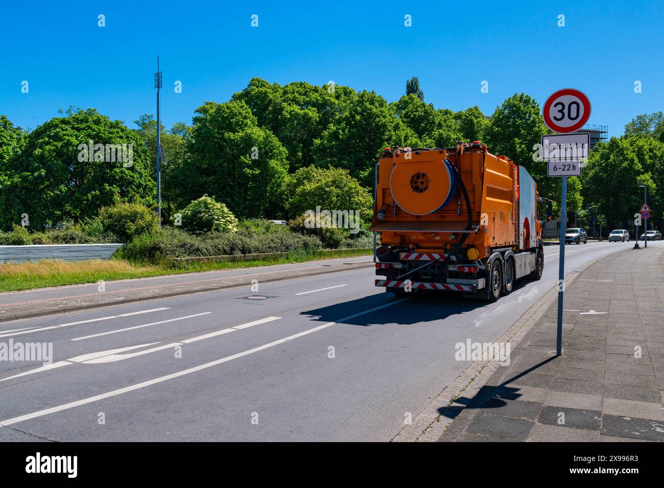 Vista posteriore di un'auto arancione per la pulizia delle fognature in ambienti urbani. Strada cittadina con auto che passano raramente Foto Stock